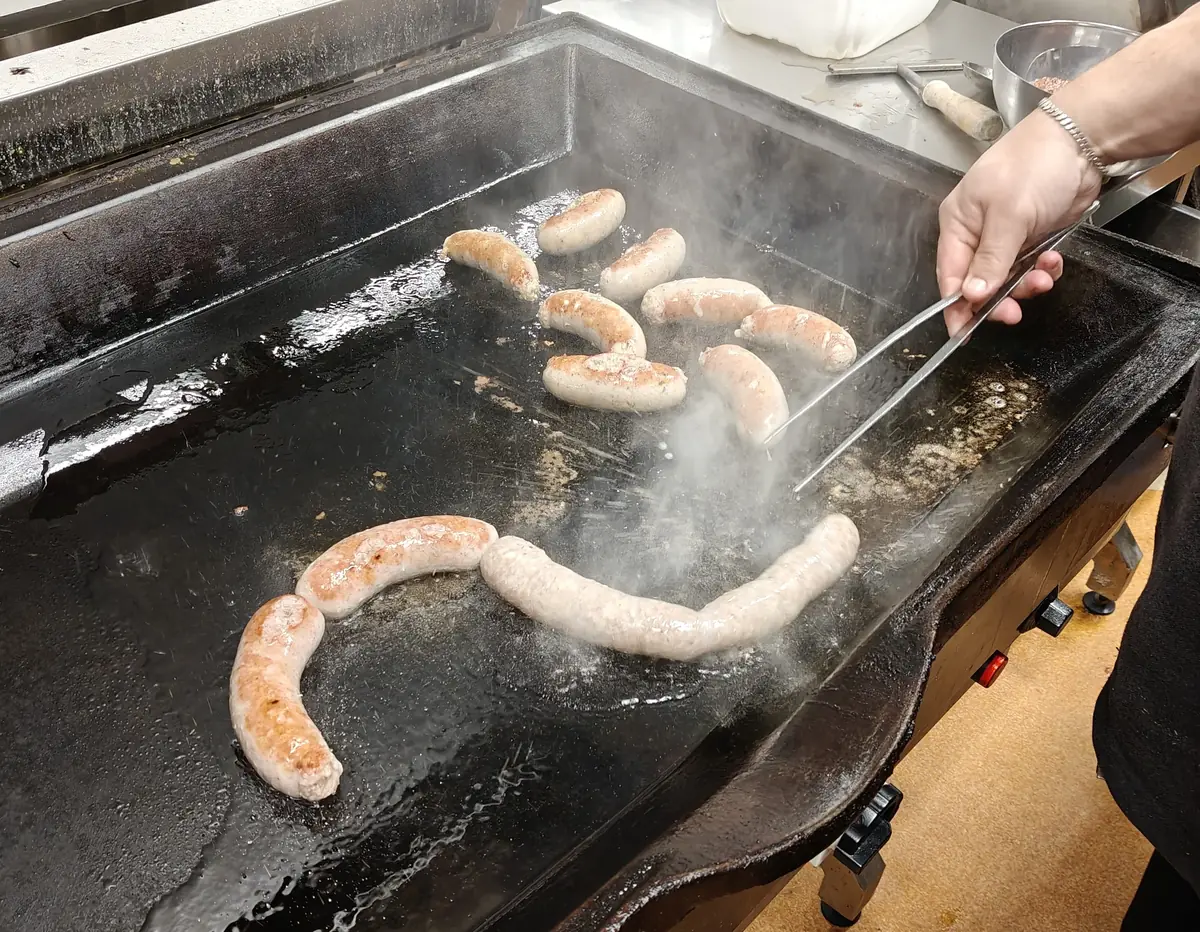 Fresh sausages sizzling on a flat-top griddle while a hand turns them with tongs