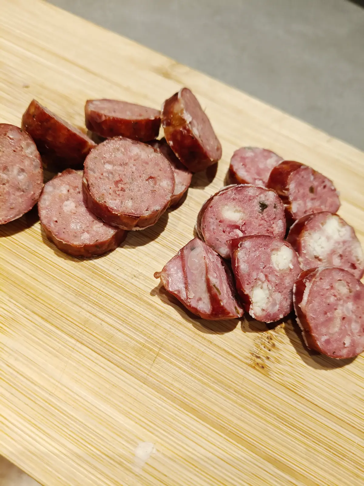 Two kinds of sausage sliced on a wooden board, the coarse texture visible in the cut