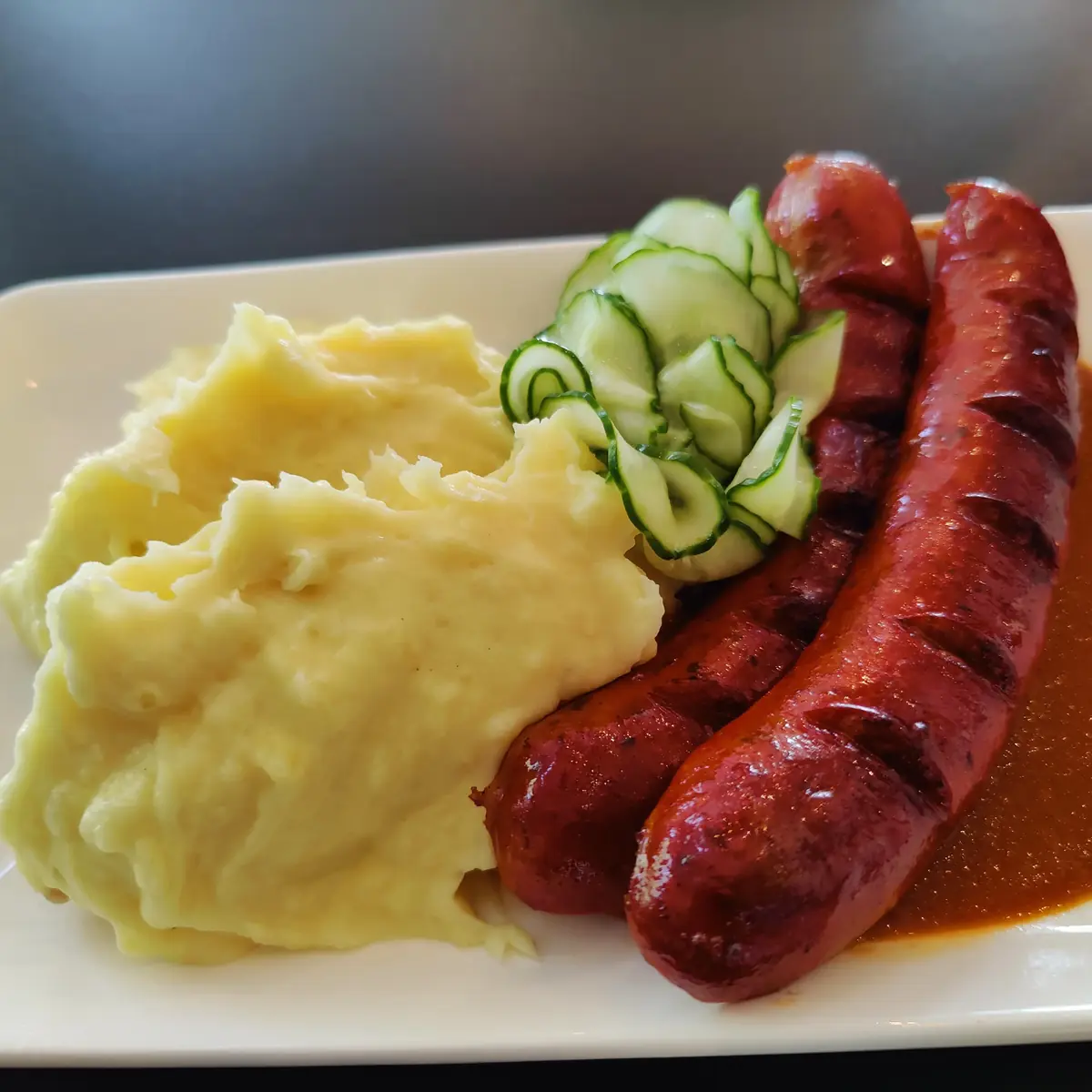 Two grilled sausages served with mashed potato and pickled cucumber