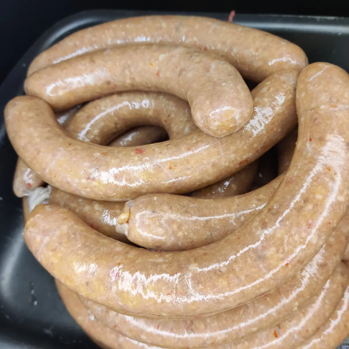 Close-up of coarsely ground raw sausages coiled in a black tray